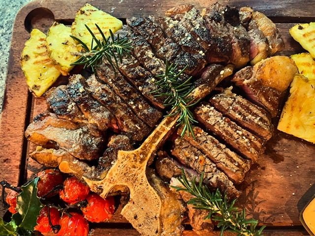 Grilled steak with herbs, pineapple slices, and cherry tomatoes on a wooden cutting board.