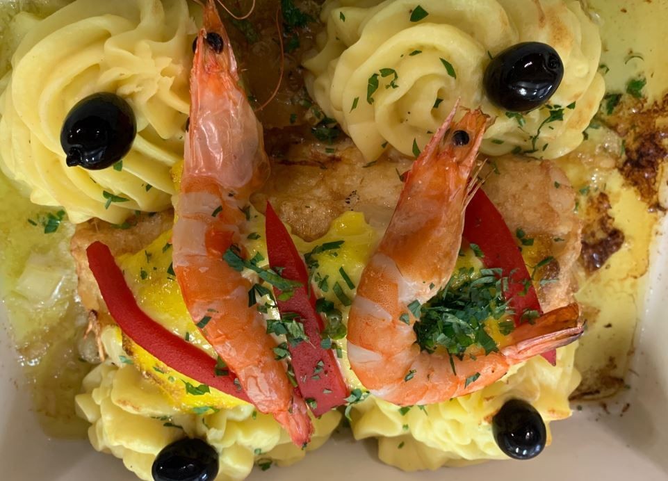 Dish with prawns, mashed potato swirls, olives, and garnished with parsley.